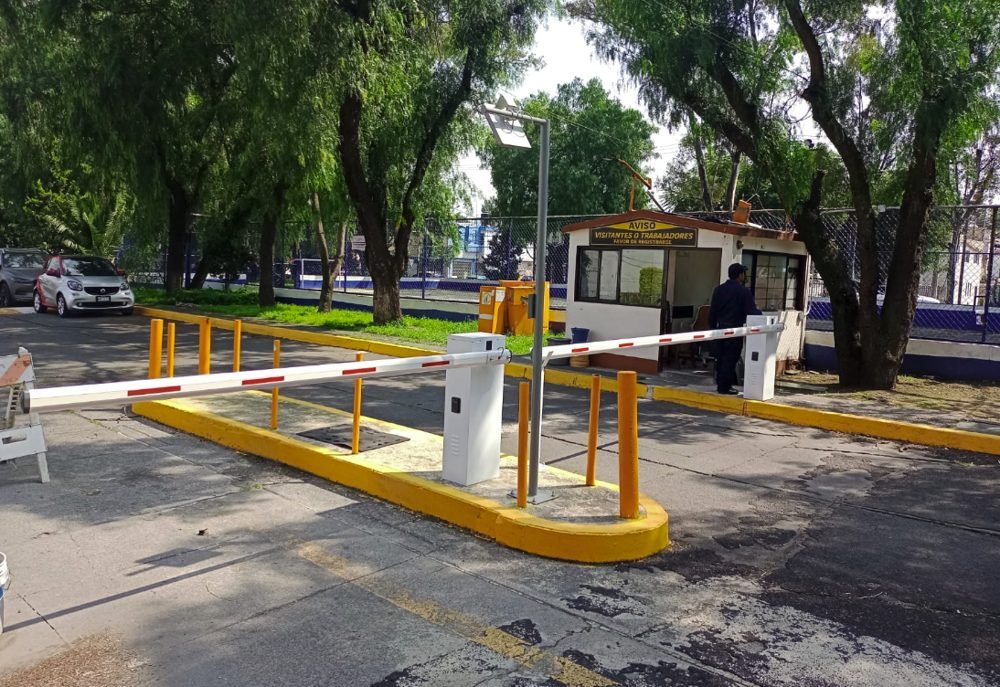 Entrada de un condominio con caseta de vigilancia y dos plumas vehiculares de entrada y salida